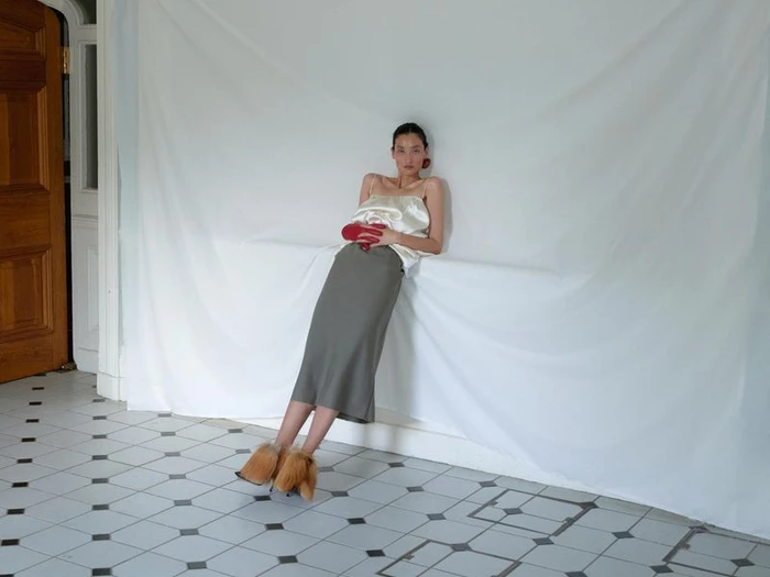 Model Lina Zhang in a satin top and skirt leaning against a draped white sheet in Holiday Magazine editorial