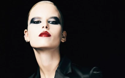 Close-up portrait of a model with dramatic dark eye makeup and glossy red lips against a black background