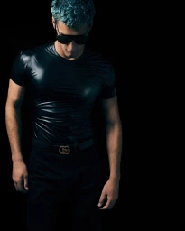 Model in black shiny t-shirt and sunglasses posing against black background for GQ Turkey