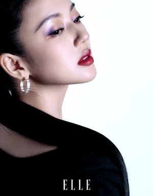 Portrait of a woman wearing silver hoop earrings with purple eyeshadow and dark red lipstick against a plain white background.