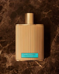 Gold fluted perfume bottle with a turquoise label resting on a dark brown marble surface