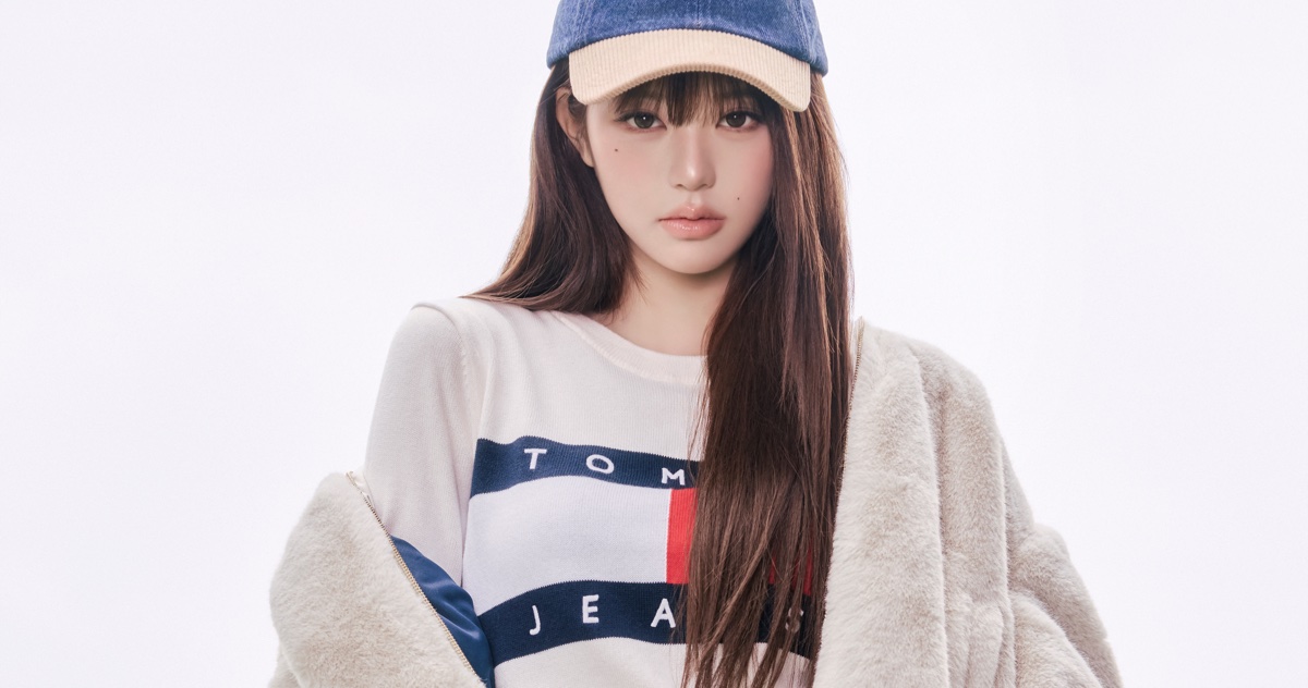 Jang Wonyoung wearing a Tommy Hilfiger logo sweater and blue cap against a white background