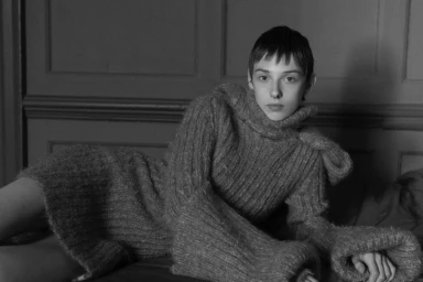 Model wearing a thick turtleneck sweater reclining against paneled walls for Numero New York