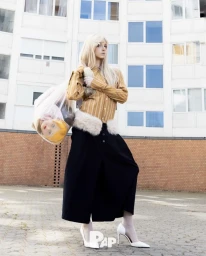 Woman in yellow striped shirt and black skirt holding a plastic trash bag with a doll head inside.