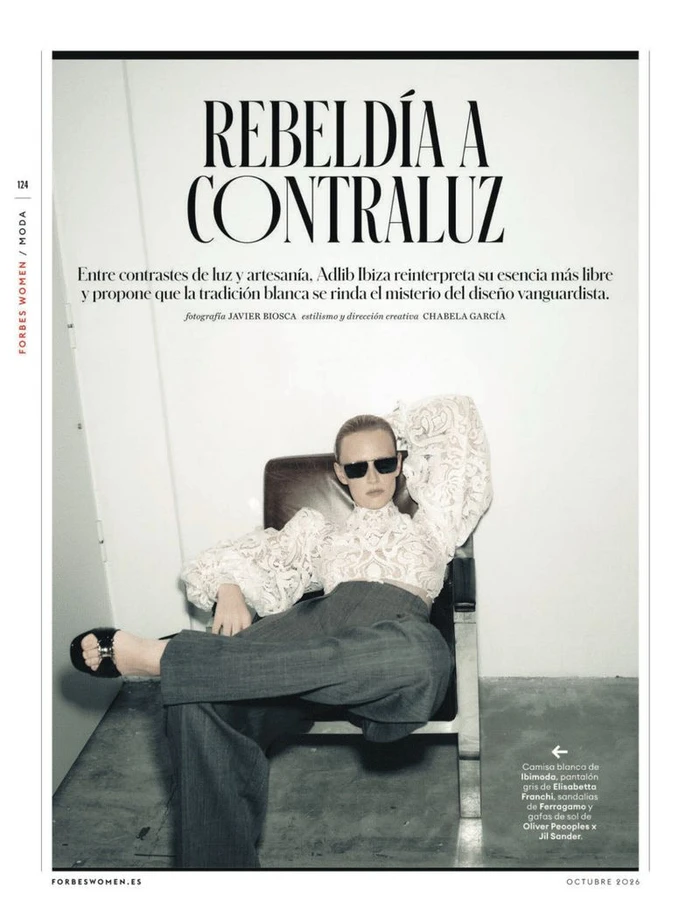 Magazine page layout featuring a model wearing dark sunglasses, white lace top, and grey trousers seated in a chair against a white background.