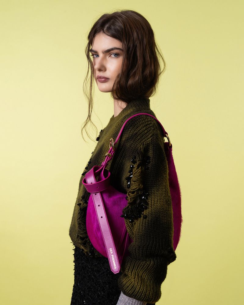 Brunette model wears a dark green sweater, black skirt, and carries a pink purse against a solid yellow backdrop in a studio shot.