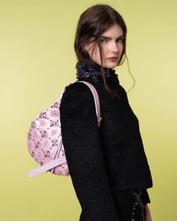 Brunette woman poses in black top and pink floral bag against yellow backdrop in a fashion studio shot for an editorial magazine spread.