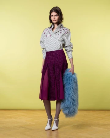 Full shot of woman in striped top and purple skirt with fur stole standing on yellow background in a fashion studio setting.