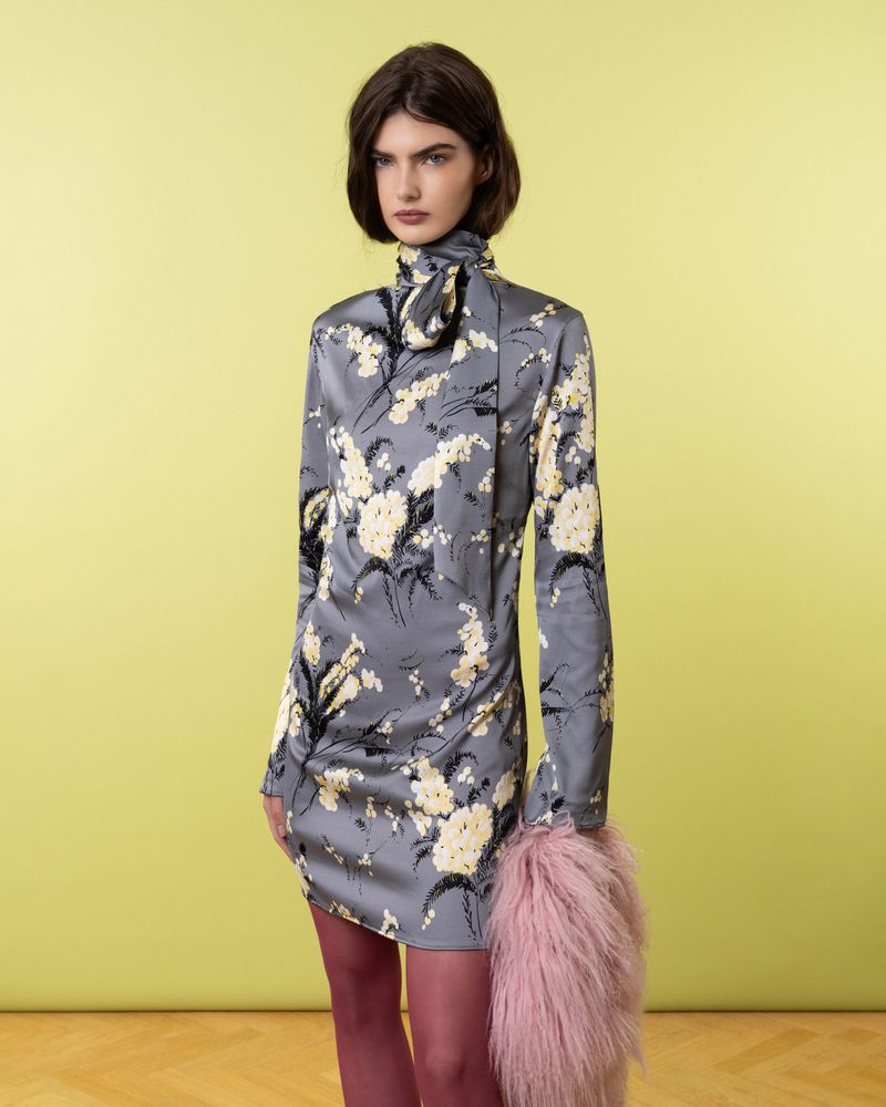 Woman in floral print dress poses against a yellow backdrop, holding a pink fur accessory. Fashion editorial with studio lighting.
