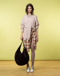 Model wearing a textured knit sweater and plaid skirt holding a large black hobo bag against a pale yellow seamless backdrop