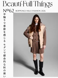 Model in brown pleated skirt, double-breasted knit sweater, beige puffer vest, and tall black boots on a grey backdrop.
