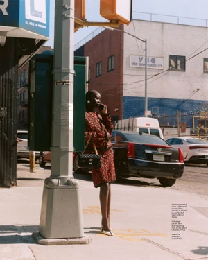 Model Aweng Chuol leaning against a street pole on a city sidewalk for Heroine Magazine