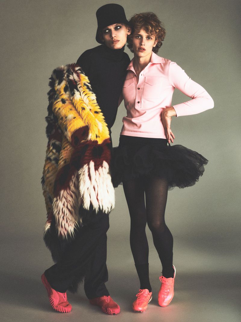 Two fashion models posing against a neutral grey studio backdrop in editorial styling for Purple Magazine.