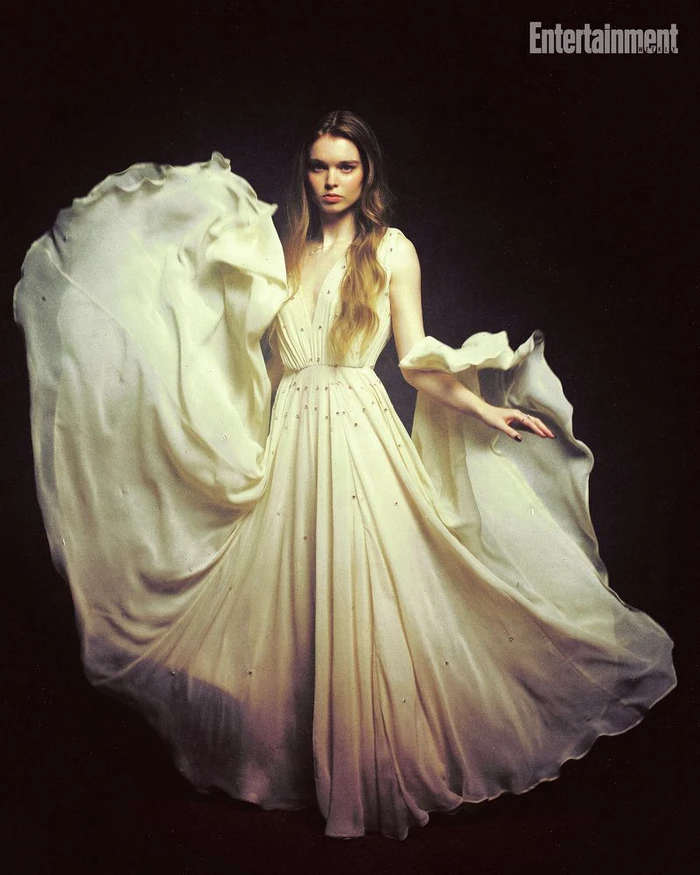 Woman in a long flowing off-white gown with flared fabric against a dark background for Entertainment Weekly.