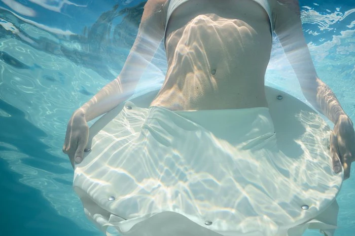 Underwater shot of a model floating in clear blue water holding a white circular object with metallic studs