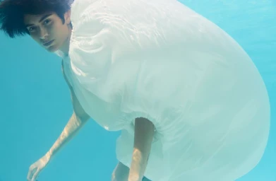 Model submerged in an azure pool wearing an inflated white garment, captured in a photographic editorial by Zoe Natale Mannella.