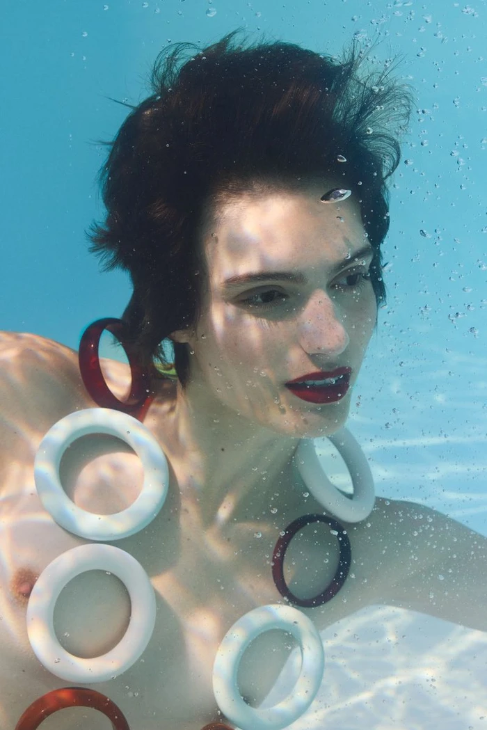 Model submerged underwater wearing large white and dark red circular accessories in a pool
