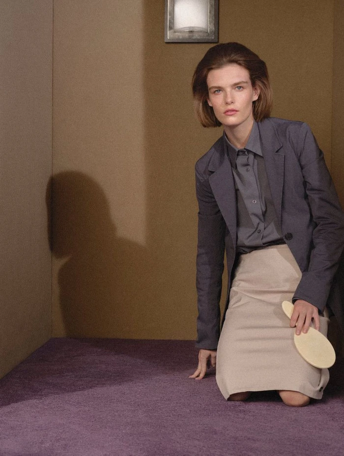 A woman in a grey blazer and skirt kneeling on a purple carpet holding a paddle