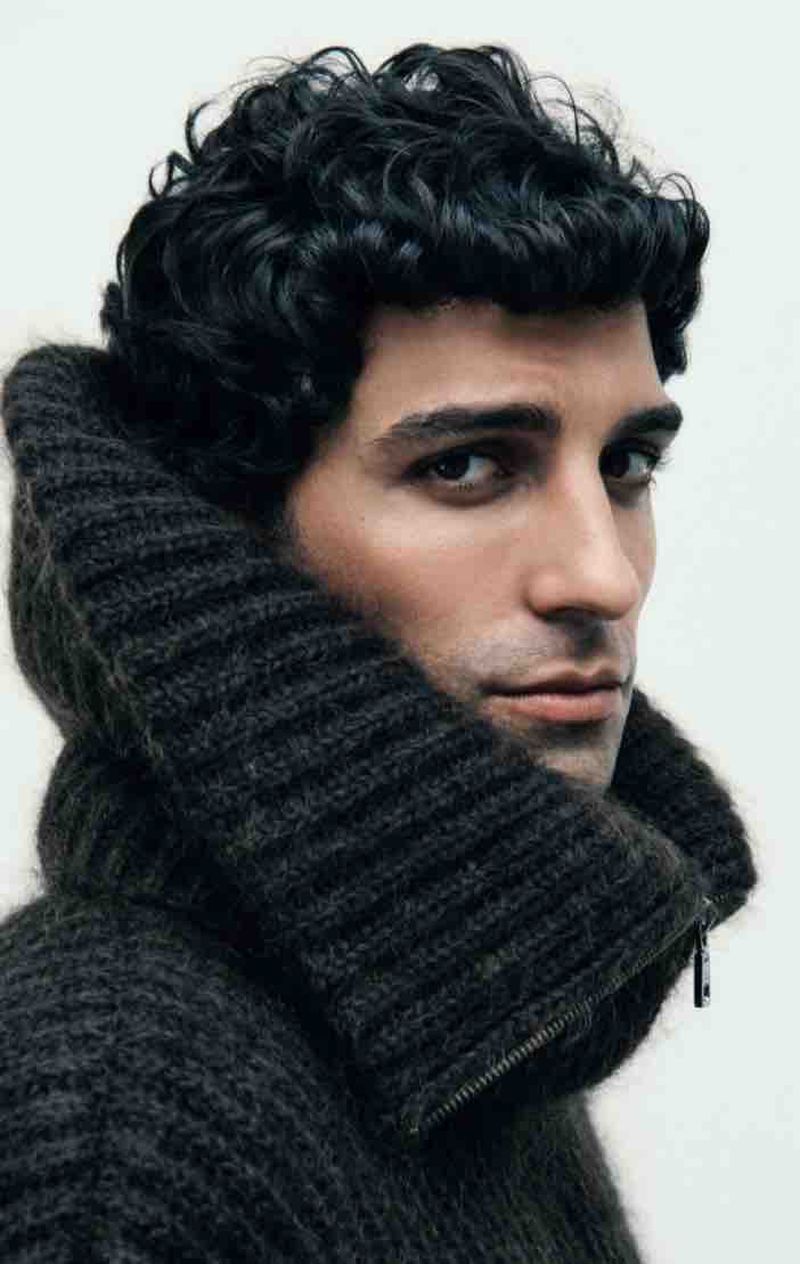 Close-up portrait of a male model wearing a dark charcoal chunky ribbed knit sweater with a high collar against a plain white background.