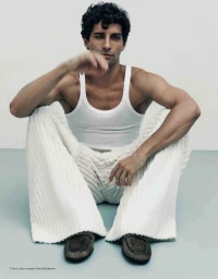 Model Francisco Faria seated on the floor wearing a white tank top and textured white trousers photographed by Guilherme da Silva