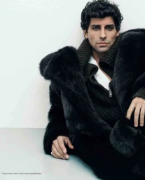 Model Francisco Faria wearing a black fur coat and ribbed collar sweater against a pale background