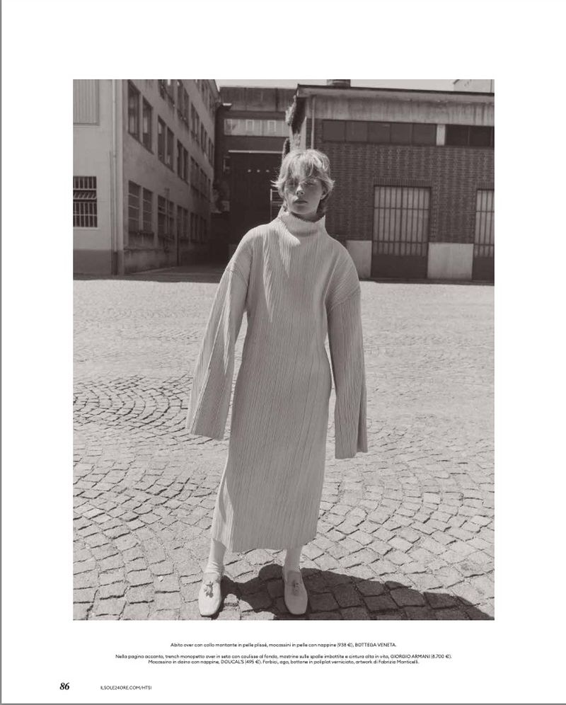 Model standing outdoors on cobblestones wearing a long textured turtleneck dress with wide sleeves.