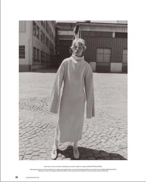 Model standing outdoors on cobblestones wearing a long textured turtleneck dress with wide sleeves.