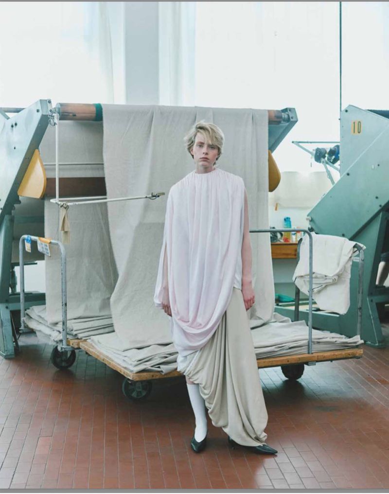 Model standing in front of large textile rolls on a rolling cart in an industrial factory setting