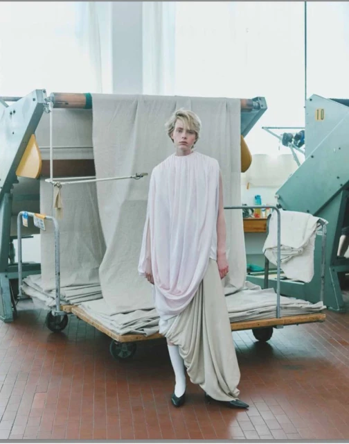 Model standing in front of large textile rolls on a rolling cart in an industrial factory setting