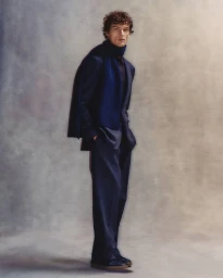 Model in navy suit and matching scarf posing against a textured grey studio backdrop for BOSS by David Beckham.
