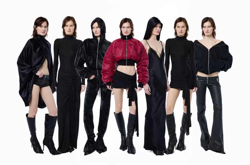 Several women stand in a bright, clean space wearing coordinated black fashion ensembles featuring dresses, tops, and boots.