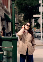Model in camel jacket and sunglasses standing outdoors by a green subway entrance for J. Crew