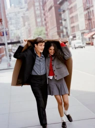 Man and woman walking together on a city street holding a brown coat over their heads as protection against weather.