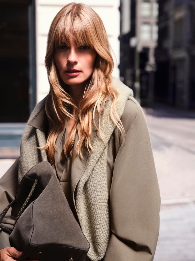 Model Julia Stegner wearing an olive coat and holding a dark handbag outdoors on a city street for BOSS.