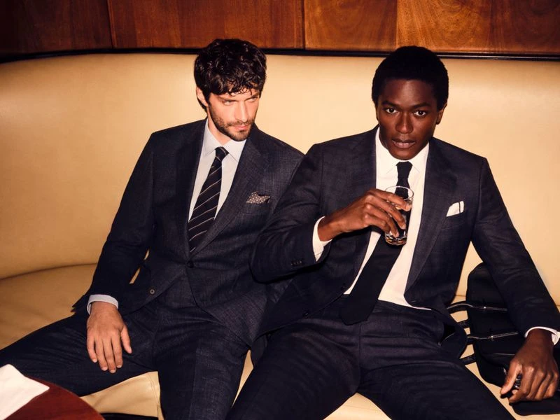 Two men in dark suits seated on a leather booth in a bar for a BOSS campaign