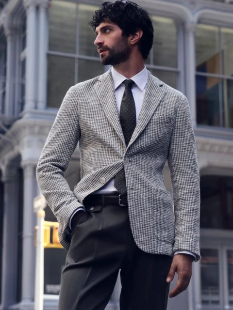 Man wearing a grey tweed blazer and dark tie standing in front of classical stone architecture.