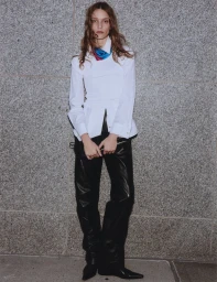 Model in a white shirt and black trousers standing against a textured stone wall for Elle Canada