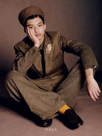 Model seated on the floor wearing a brown tweed suit and hat, resting chin in hand for Vogue China Men editorial.