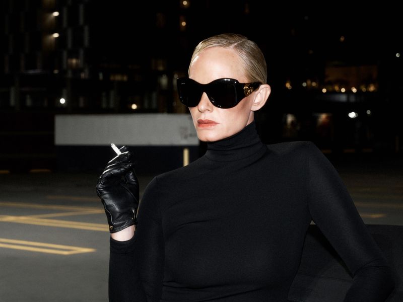 Amber Valletta in sunglasses and black turtleneck holding a cigarette in black leather gloves at night