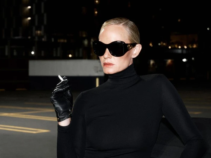 Amber Valletta in sunglasses and black turtleneck holding a cigarette in black leather gloves at night