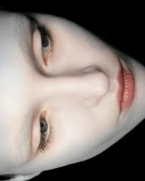 Close-up vertical portrait of a woman with pale skin, muted lips, and dark eyelashes against a black background.