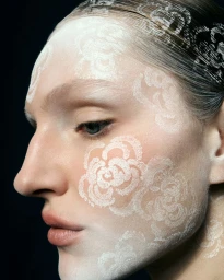 Close-up profile portrait of a woman with white floral lace patterns painted across her face and head for Tush Magazine.