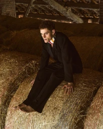 Model Slava Sikorski in a black suit sitting on hay bales in a barn for Vanity Teen Magazine