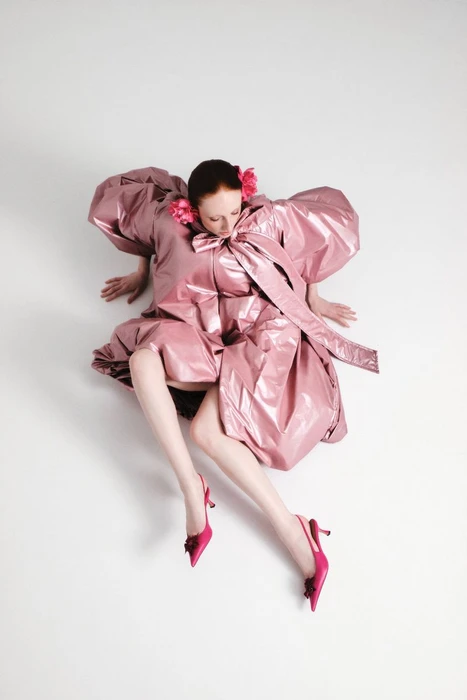 Model wearing a metallic pink puffed-sleeve dress and pink heels sitting against a plain white background