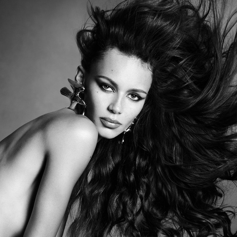 Model Binx Walton with flowing dark hair and sculptural silver earrings in a black and white fashion portrait.