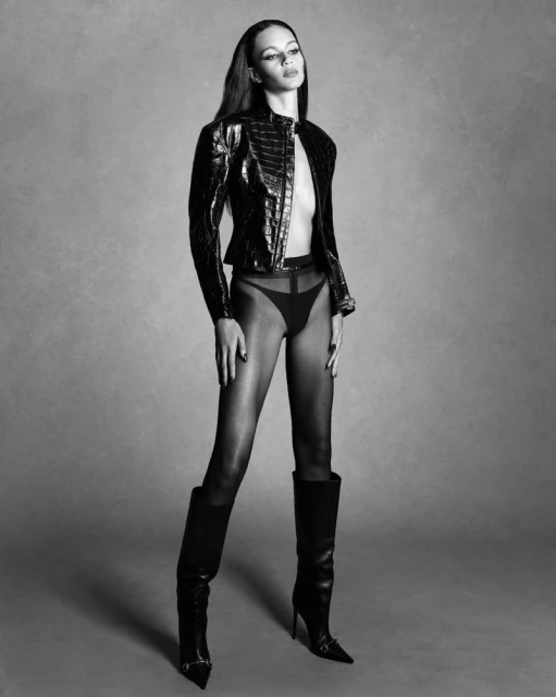 Model Binx Walton in a black textured jacket and high boots against a plain grey studio backdrop for Double Vision.