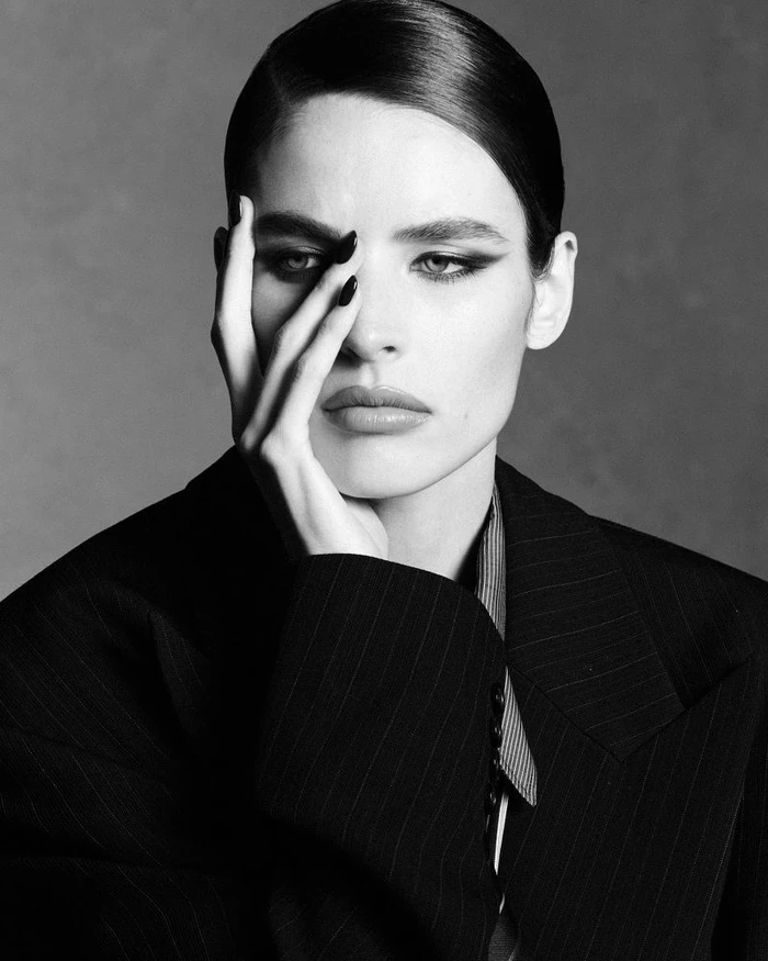 Monochrome portrait of model Libby Taverner posing with hand near face wearing a dark pinstripe blazer for Double Vision.