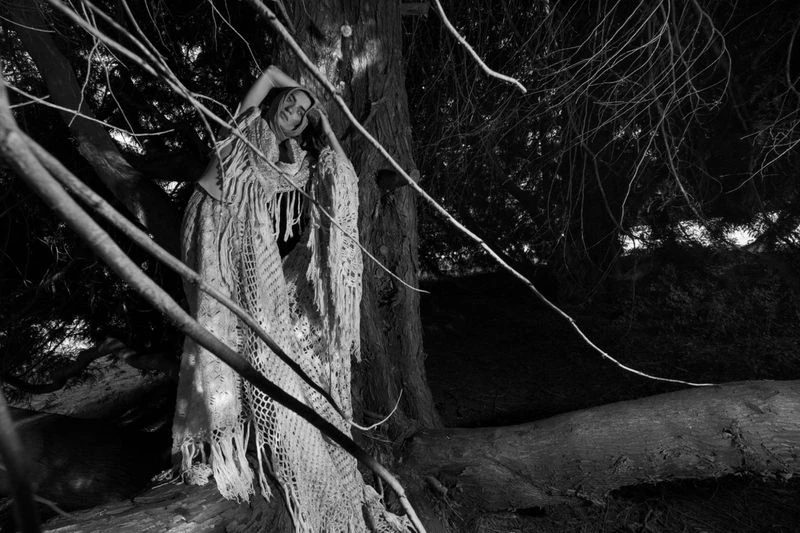 Model Isa Nilwik in a textured knitted dress leaning against a tree trunk in a dark woodland captured by Inez and Vinoodh.