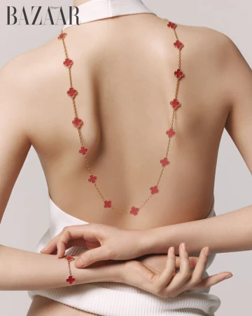 Back view of a woman wearing a white top and a long gold necklace with red clover motifs for Harper's Bazaar Korea
