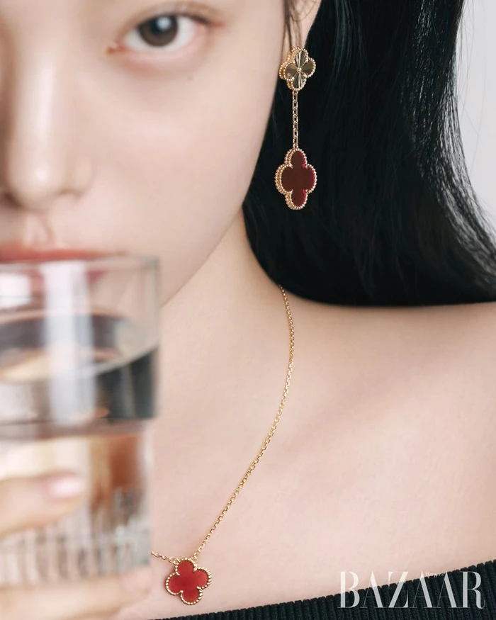Close-up portrait of a woman wearing clover-shaped pendant earrings and necklace holding a glass of water for Harper's Bazaar Korea